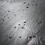 A photograph of a beach of black sand, dotted with smooth black pebbles.