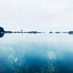 A photograph of a simple ocean landscape, with a person walking between the water and sky.