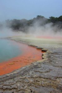 A photograph of an otherworldly lake with bright blue water and an orange shore.