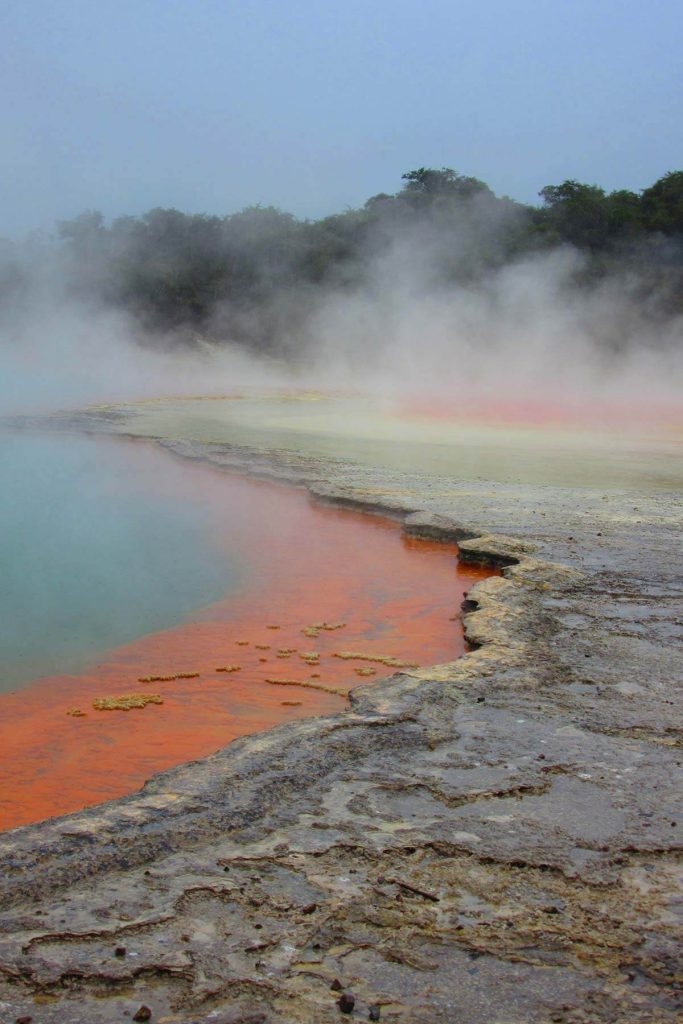 A photograph of an otherworldly lake with bright blue water and an orange shore.