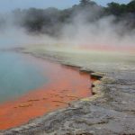 A photograph of an otherworldly lake with bright blue water and an orange shore.