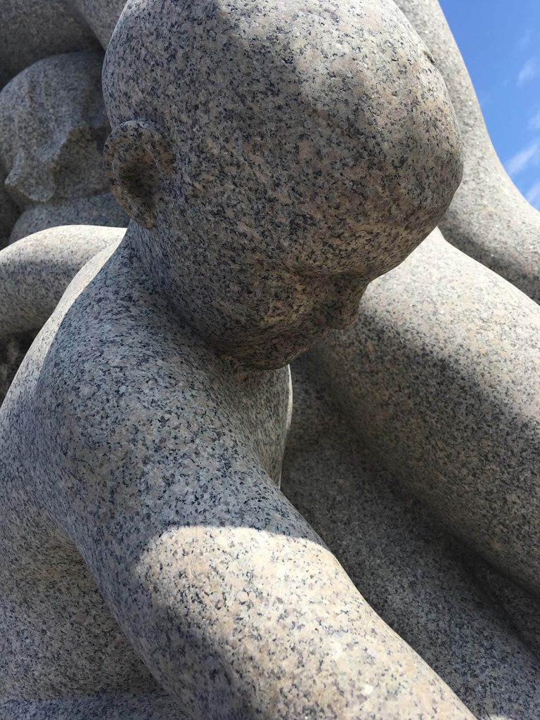 Photograph of human-shaped rock sculpture looking down.