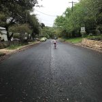 A photograph of a girl in a rainbow shirt, biking down a hill.