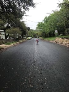 A photograph of a girl in a rainbow shirt, biking down a hill.