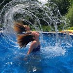A photograph of twin girls in a pool flicking their water-soaked hair in an arc.