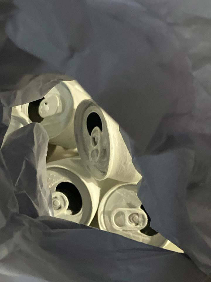 A mixed media image of aluminum cans painted white, seen through crinkled grey paper.