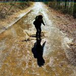 A photograph of a child splashing in a muddy puddle.