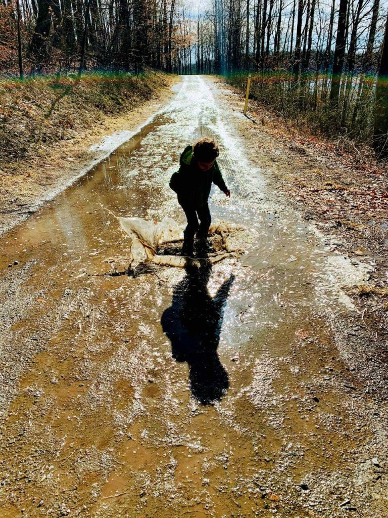 A photograph of a child splashing in a muddy puddle.